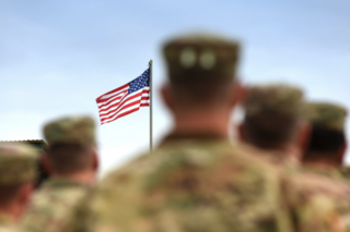 A row of service members look at an American flag in the distance.