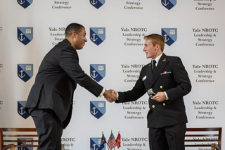 A student in uniform shakes hands with a guest speaker.