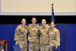 A group of cadets pose for a group photo in front of an American flag.